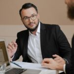 Two businessmen in a meeting discussing strategies with laptops and documents.